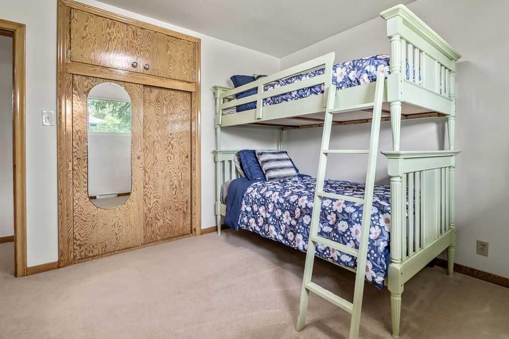 Bedroom with white bunk bed, blue bedding, and mirrored wardrobe on beige carpet.