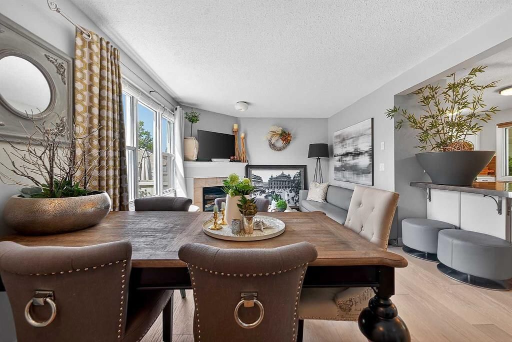 Bright dining room with wooden table, tufted chairs, fireplace, wall art, and large windows