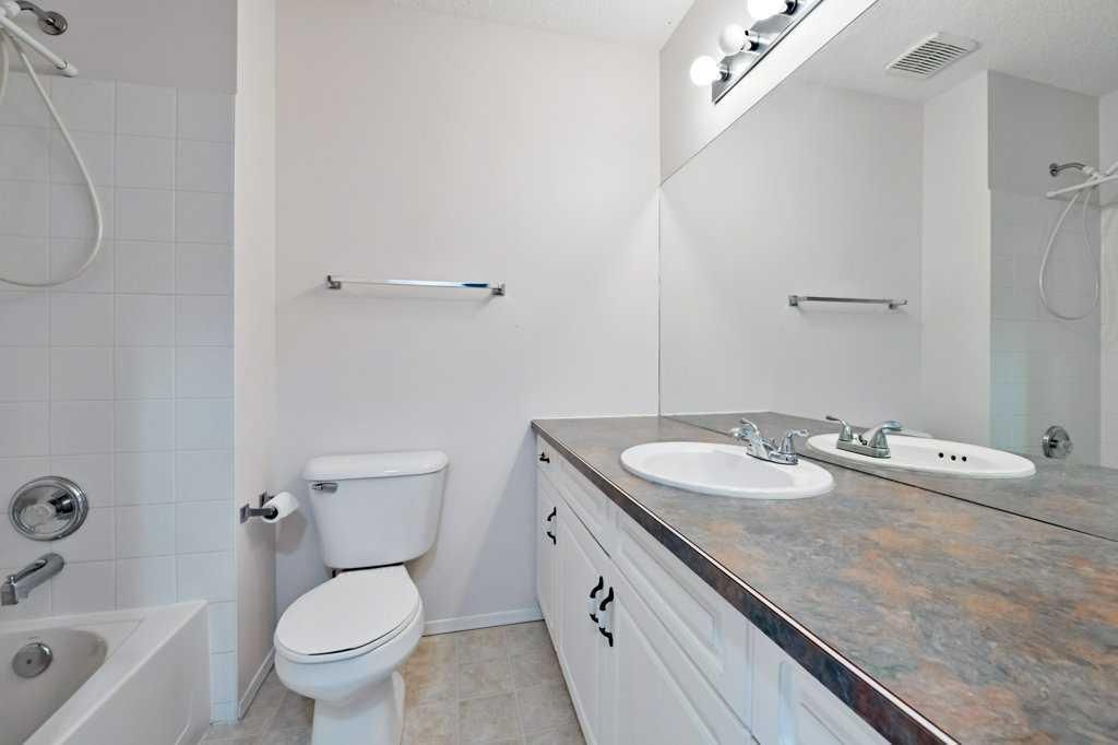 Bright bathroom with toilet, bathtub, and double vanity with granite countertop and mirror.
