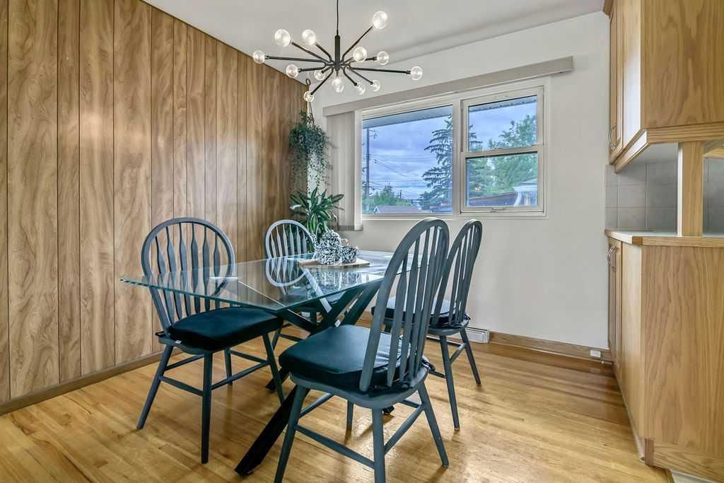 Dining room with wooden cabinets, black chairs, and a glass table by a bright window.