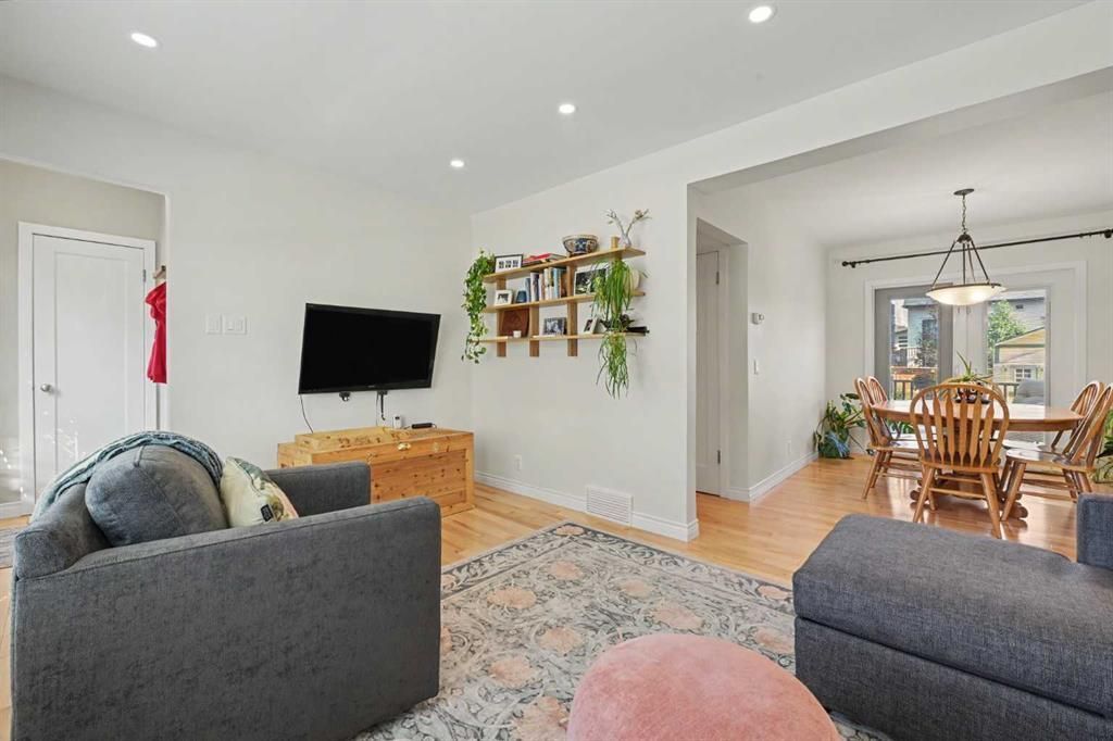 Bright living room with gray sofas, wall-mounted TV, patterned rug, and adjoining dining area.