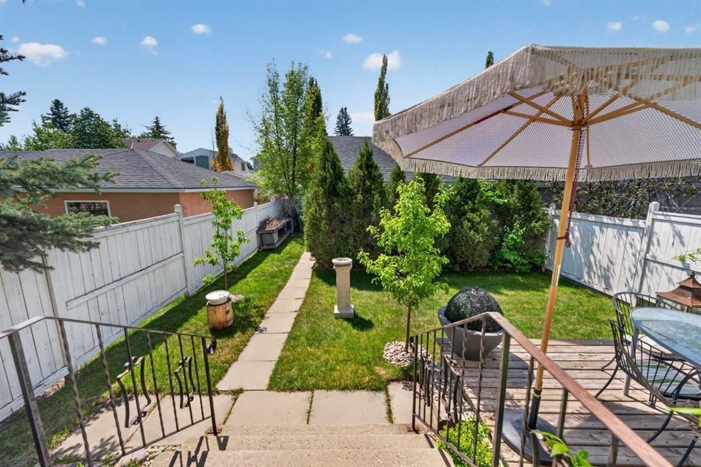 Backyard patio with a central lawn path, black iron railing, and a large umbrella beside a white fence