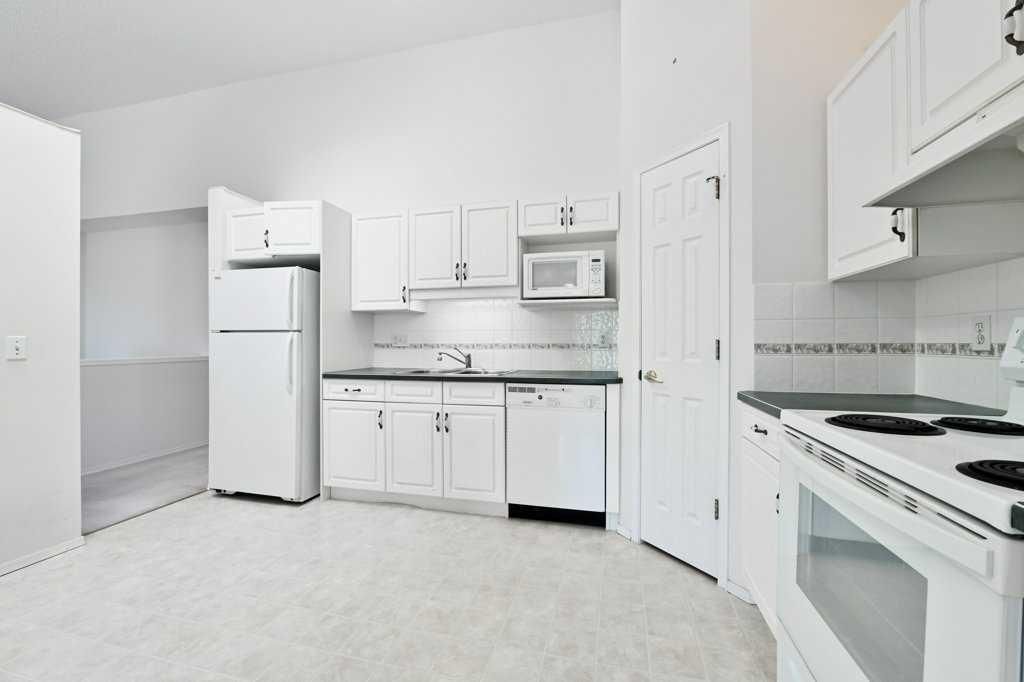 Bright white kitchen with refrigerator, stove, microwave, cabinets, and tiled floor