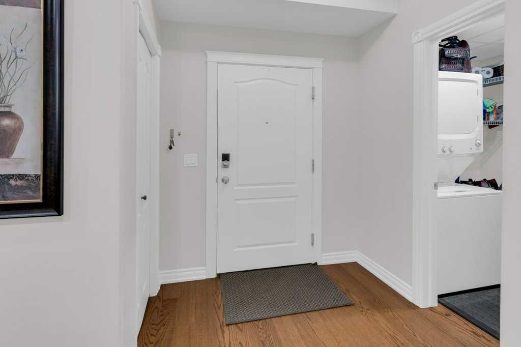 Hallway with white front door, gray rug, and hardwood floor; kitchen doorway visible on the right