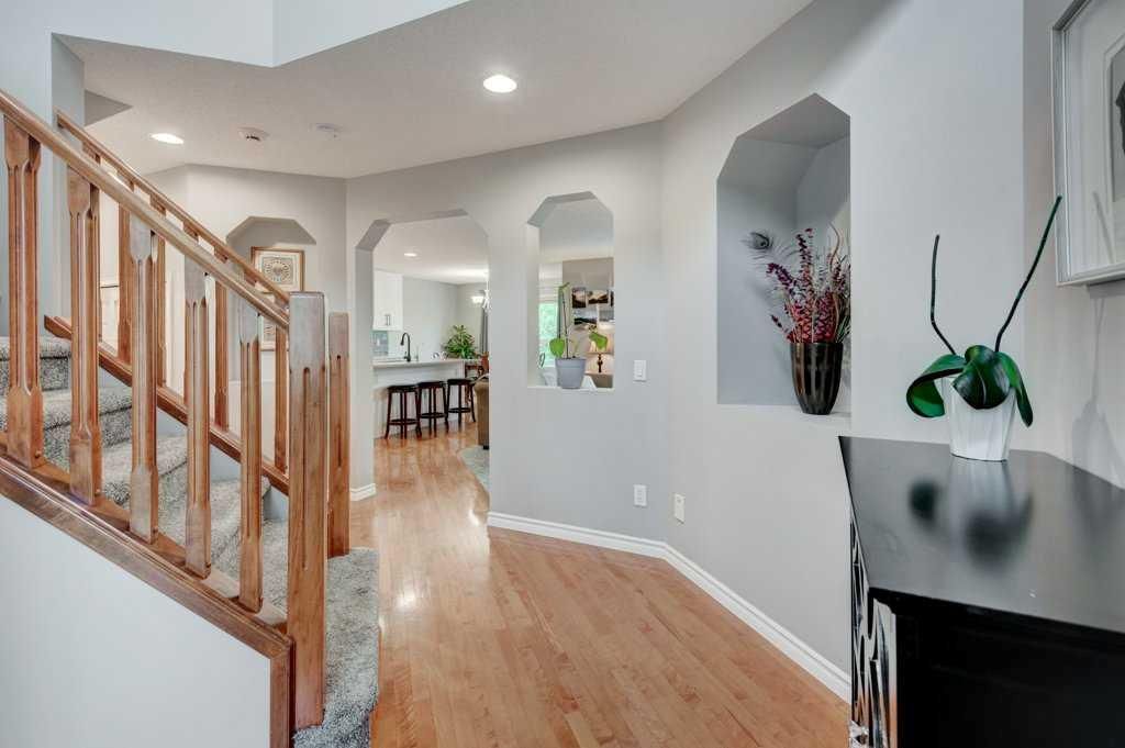 Bright hallway with hardwood floors, staircase, arched openings, and a black cabinet with a plant