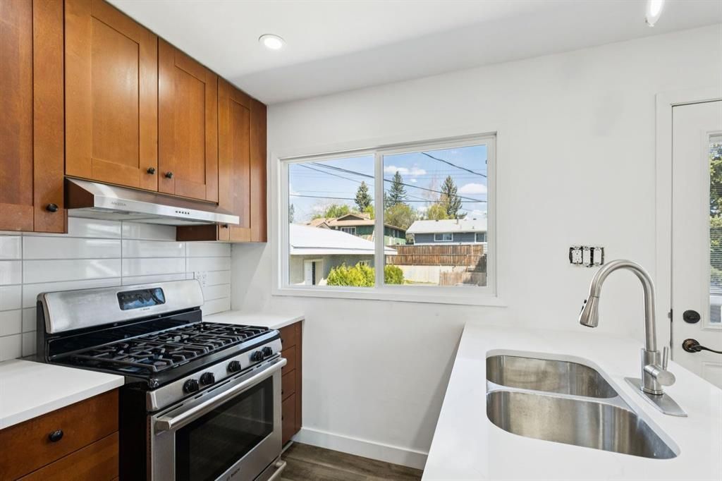 Bright kitchen with wooden cabinets, white countertops, stainless stove, sink, and window view