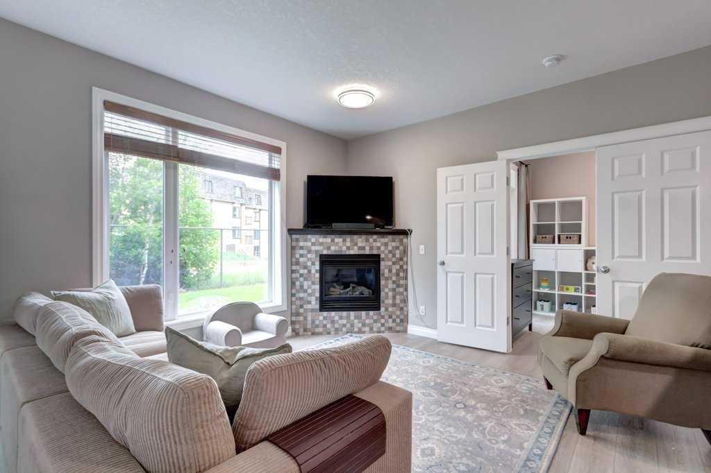 Modern living room with fireplace, TV, armchair, gray sofa, and open kitchen in the background
