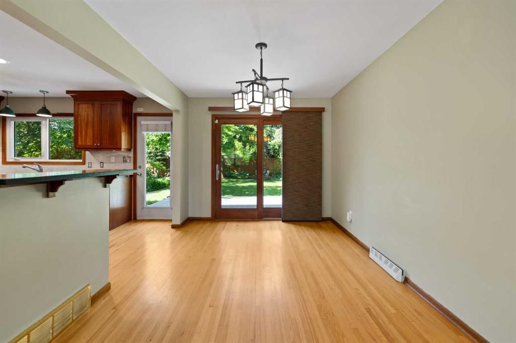 Empty dining room with hardwood floors, chandelier, and French doors opening to a green backyard.