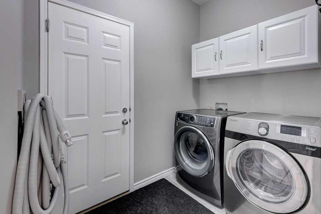 Laundry room with stacked washer and dryer, white cabinets, and a door with hanging towels.