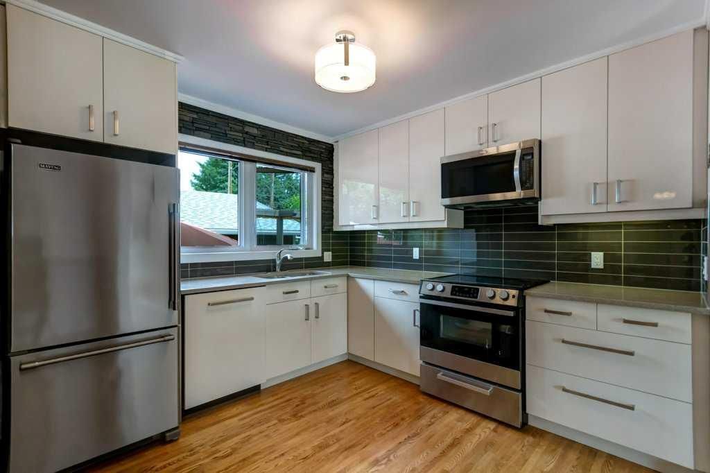 Bright modern kitchen with stainless steel appliances, white cabinets, green backsplash, and a window above the sink