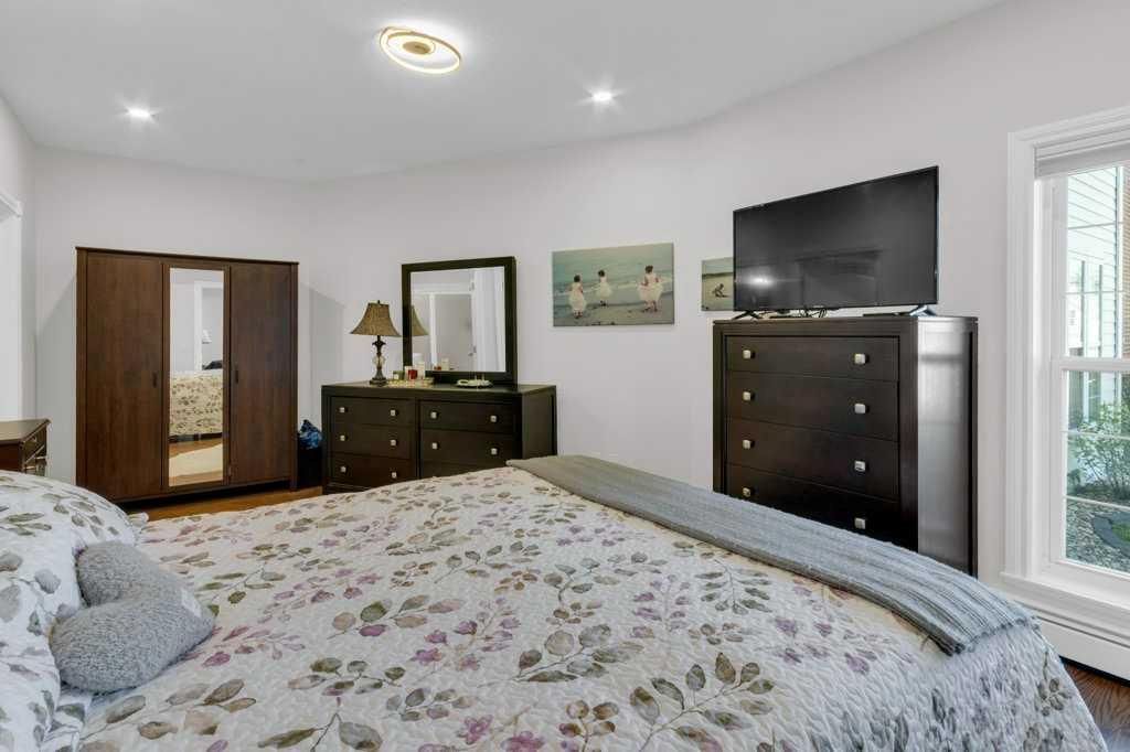 Bright bedroom with floral bedspread, dark wood furniture, wall mirror, TV, and large windows