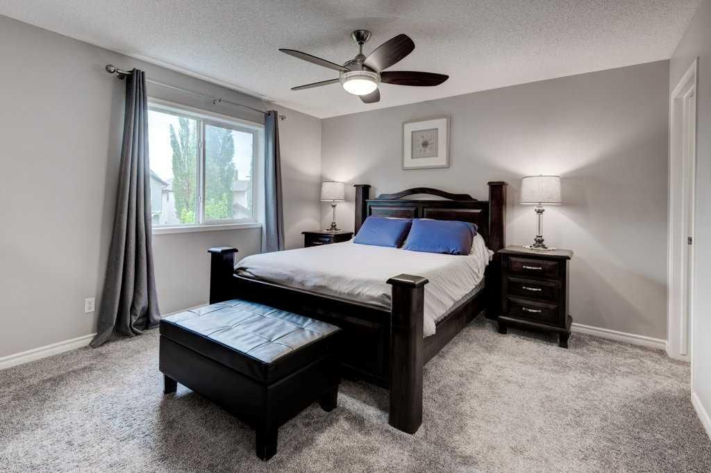 Bright bedroom with a dark wood bed, gray carpet, bench, window, and ceiling fan