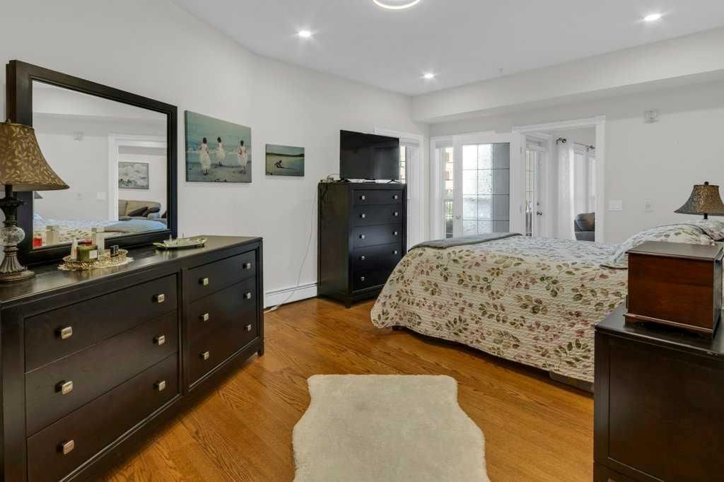 Bright bedroom with bed, dresser, dark cabinet, white rug, and hardwood floors