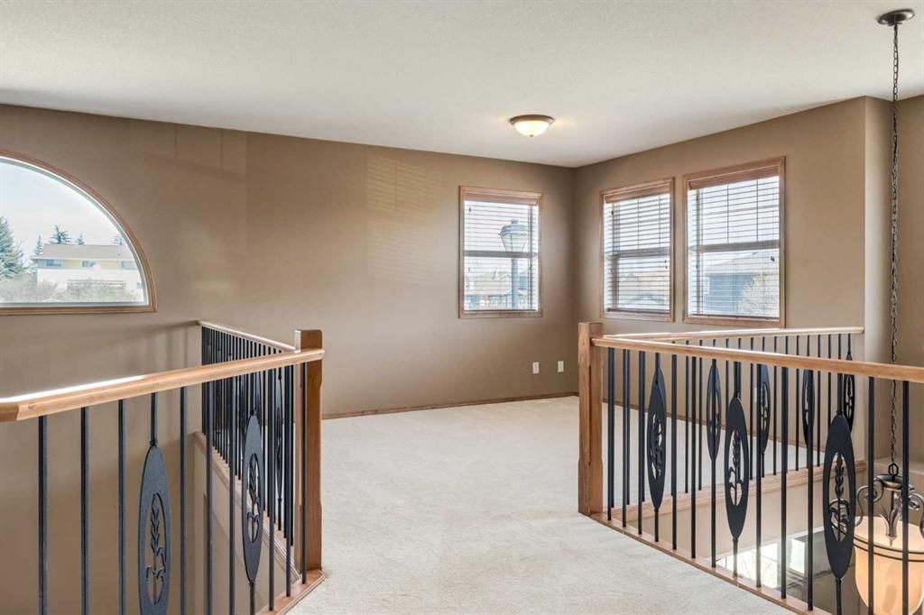 Spacious beige upstairs hallway with carpet, wood railings, and large windows letting in natural light