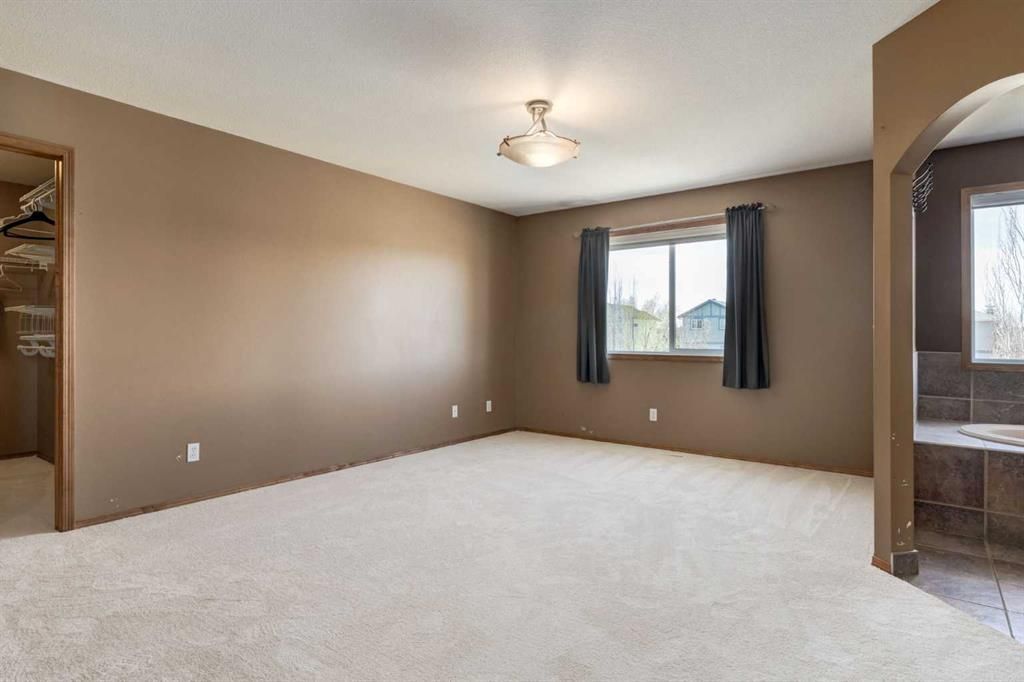 Empty beige bedroom with carpet, a window with dark curtains, and an arched doorway to a bathroom.
