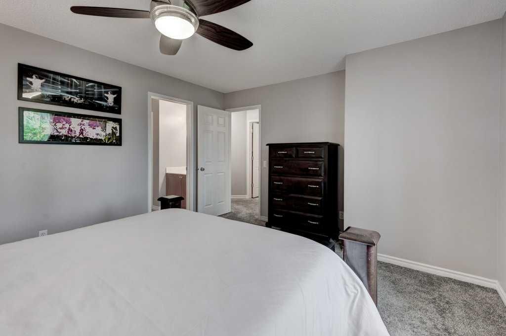 Bedroom with white bedspread, ceiling fan, mirrored closet doors, and dark dresser against gray walls