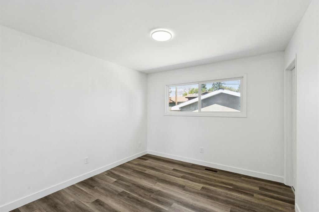 Empty white room with wood-look flooring and a small window.