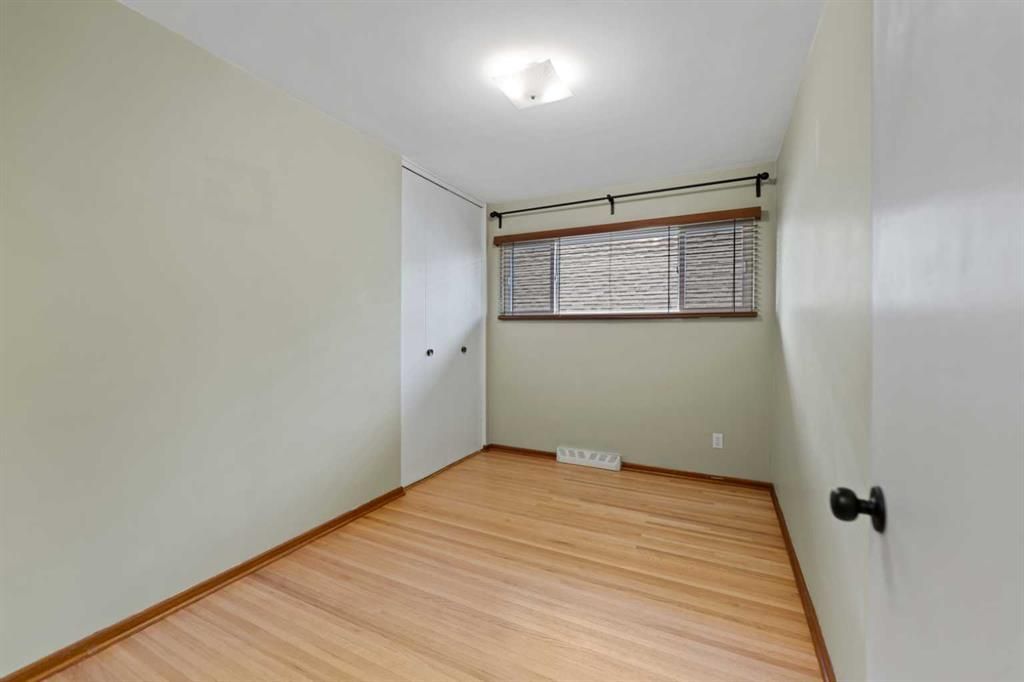 Empty small room with light wood floor, white walls, closet doors, and a window with blinds.