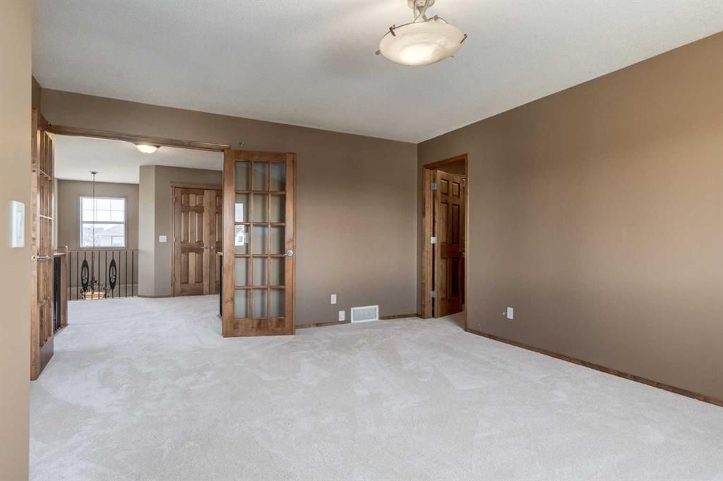 Empty beige living room with white carpet, French doors, and a hallway view