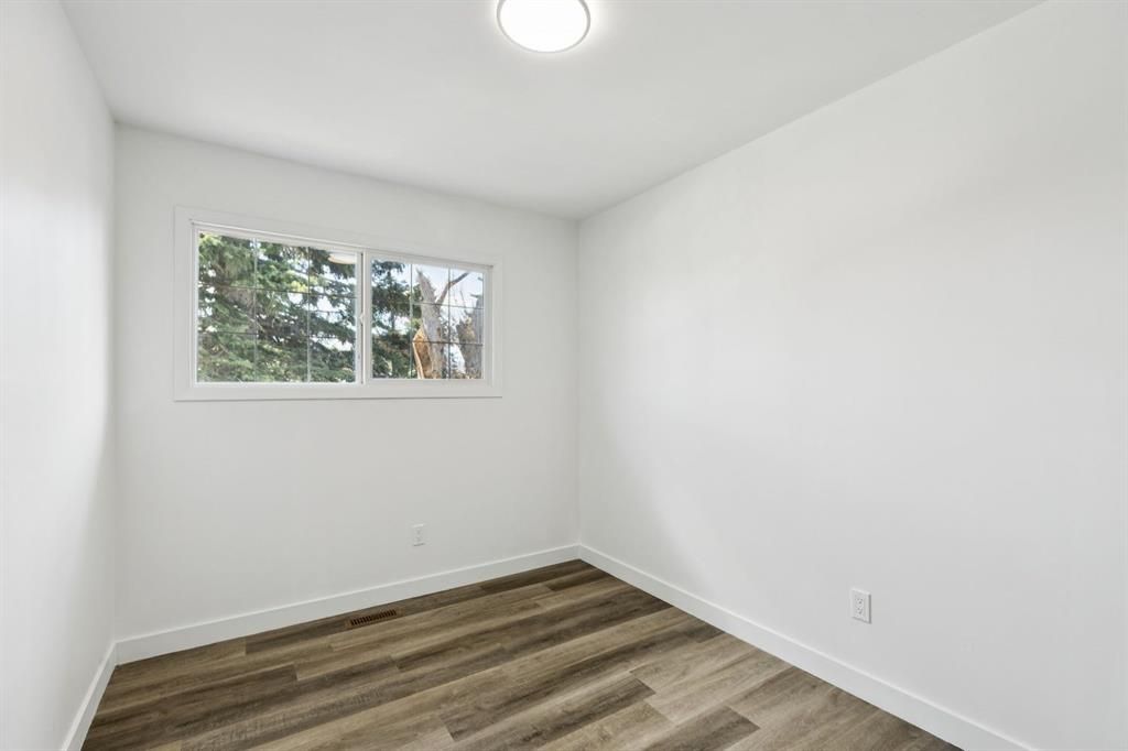 Small empty white room with a window, ceiling light, and wood-patterned floor.
