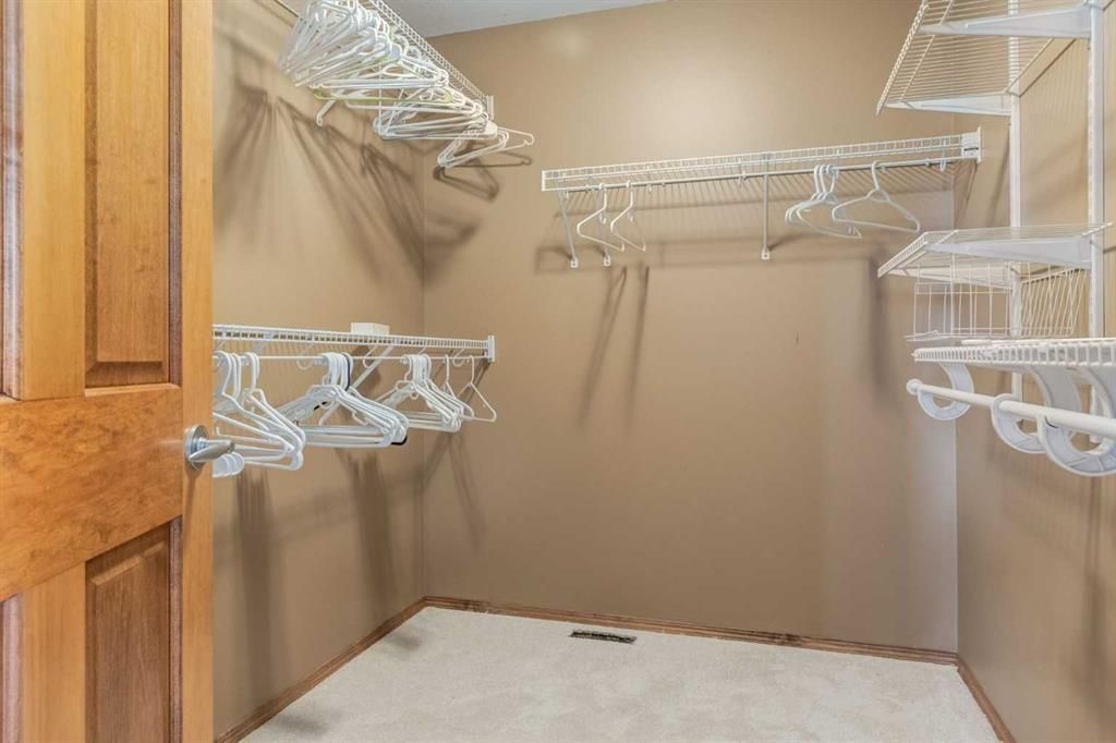 Empty walk-in closet with white wire shelves and hanging rods, beige walls, and a wood door.