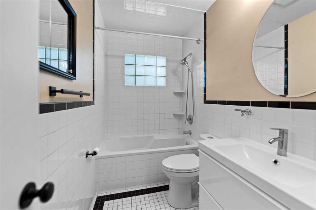 Bright white bathroom with bathtub, toilet, sink, mirror, and tiled walls
