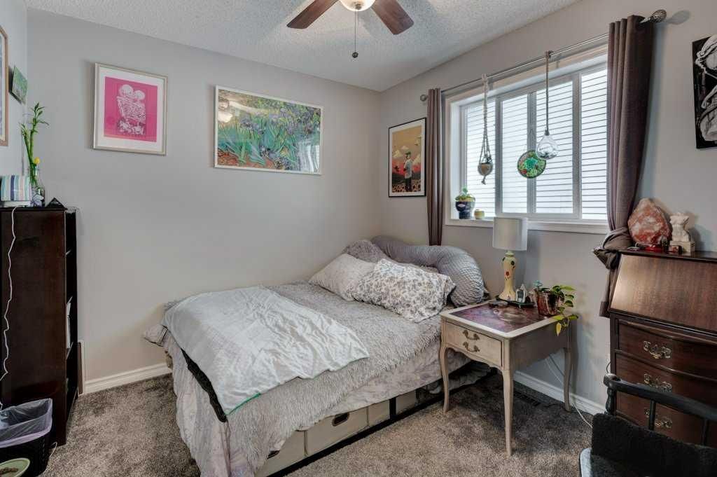 Small bedroom with a made bed, gray walls, window blinds, and a dresser with decor