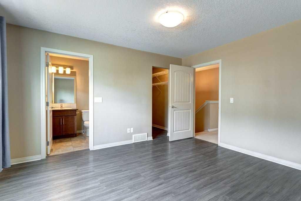 Empty bedroom with gray wood floors, beige walls, open closet door, and bathroom entrance visible.