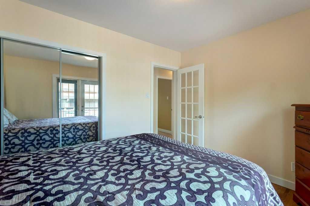 Bedroom with patterned bedspread, mirrored closet doors, and open French doors to a hallway