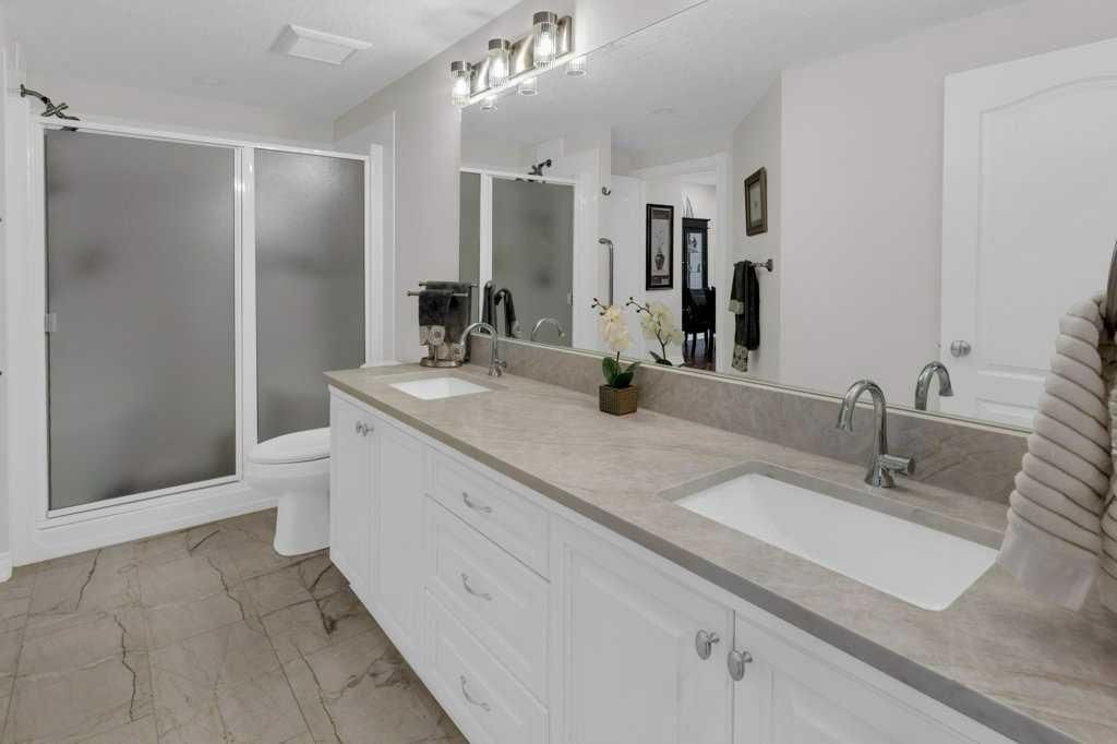 Modern bathroom with double vanity, large mirror, and frosted glass shower doors