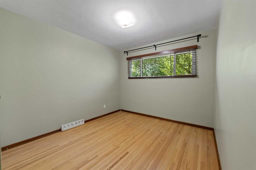 Empty light-gray room with wood floor, small window, and ceiling light