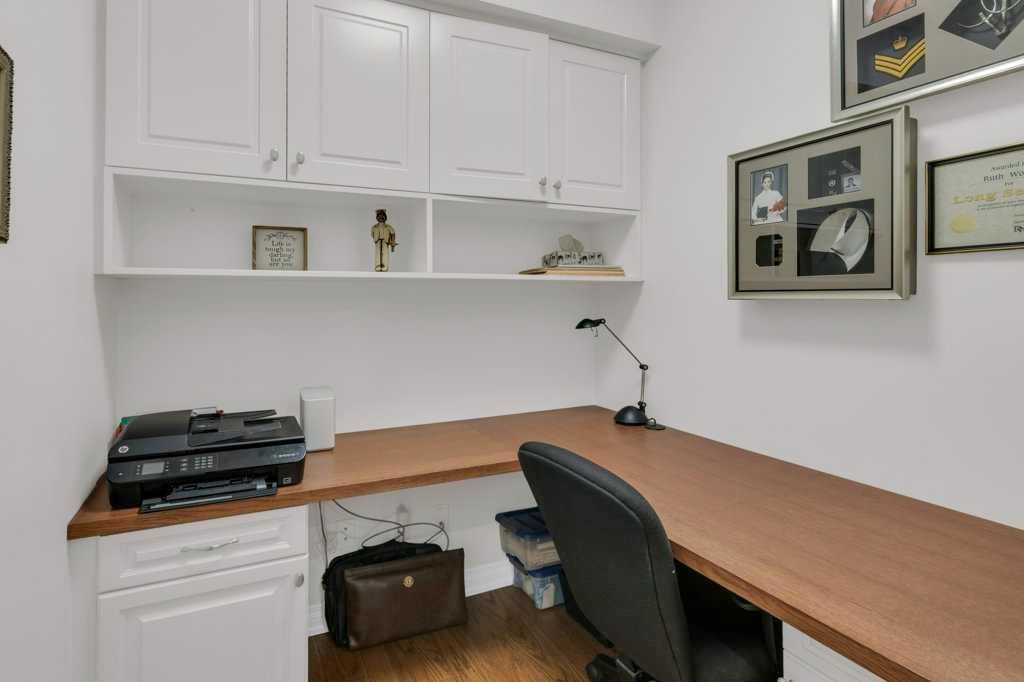 Small office with white cabinets, wood desk, black chair, and framed wall art.