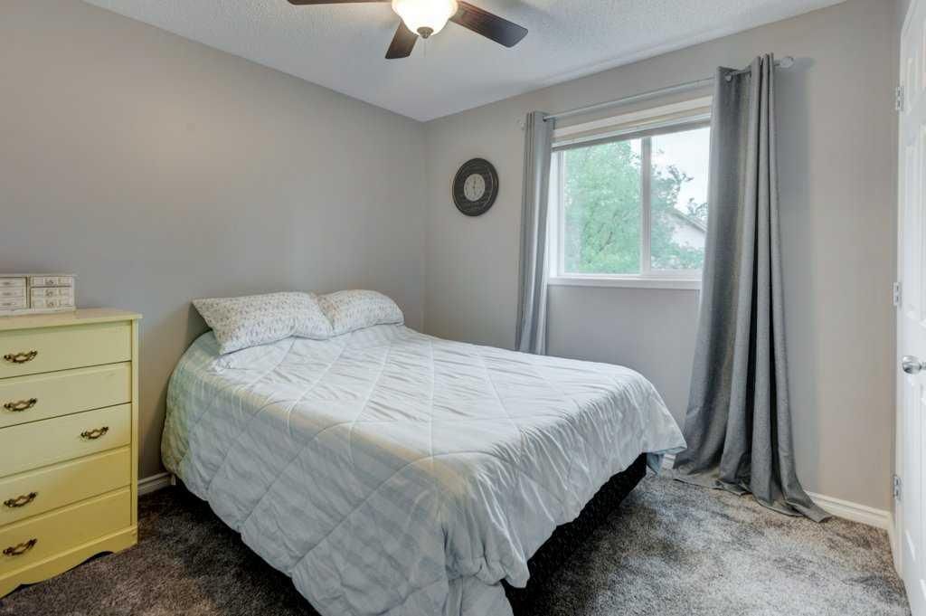 Small bedroom with a white bed, yellow dresser, window, gray curtains, and carpeted floor.