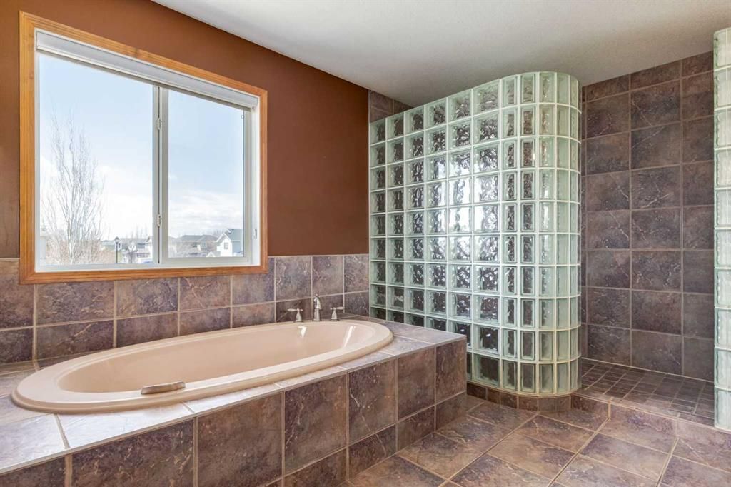 Large tiled bathroom with soaking tub, walk-in glass-block shower, and window on the left.