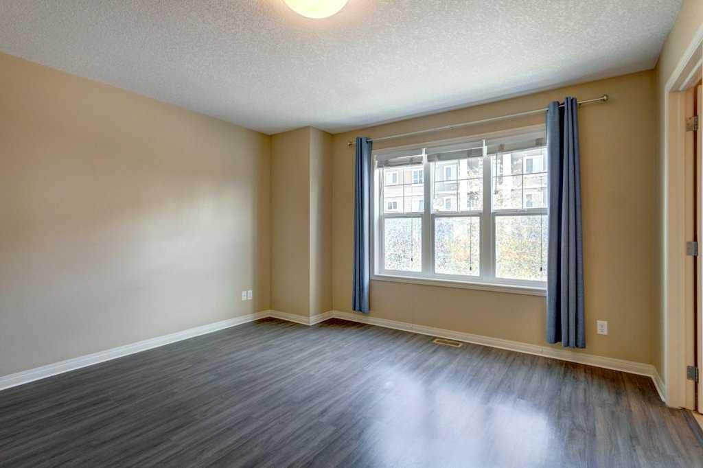 Empty beige room with dark wood floors and a large window with blue curtains