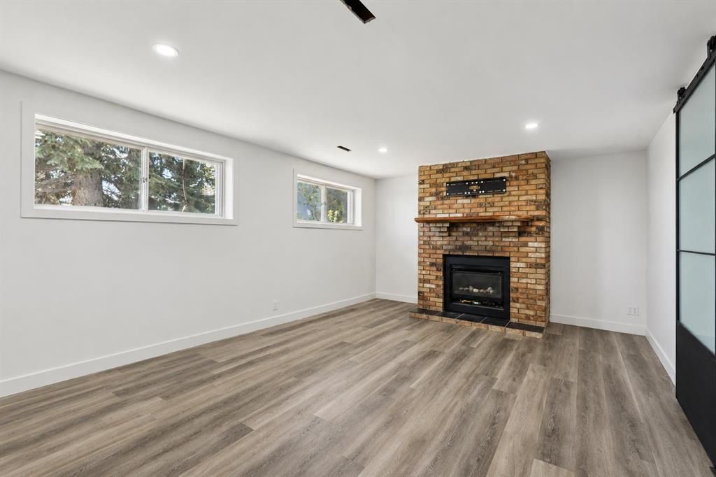 Empty living room with white walls, wood-look floor, small windows, and a brick fireplace.