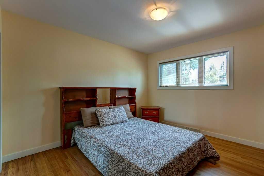 Empty bedroom with a wooden bed, floral bedding, beige walls, and a small window.