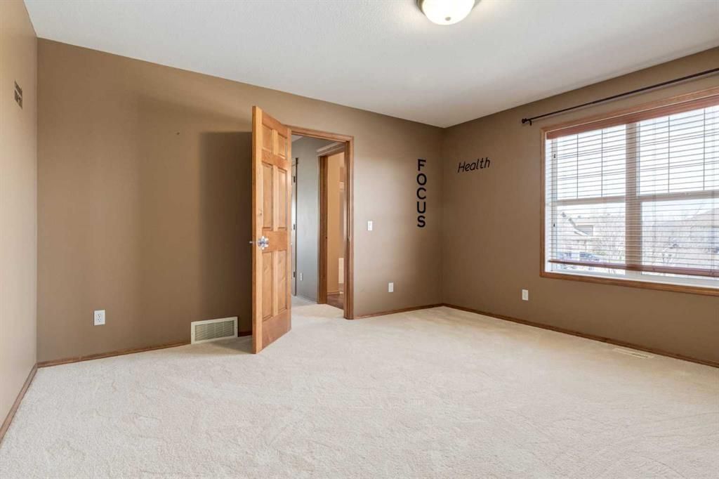 Empty beige bedroom with carpet, open door, and large window with blinds