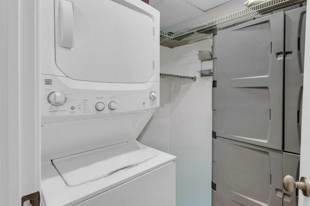 Laundry closet with stacked washer and dryer and white storage cabinets in a narrow utility space