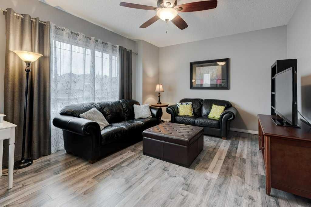 Living room with black sofas, coffee table, TV, lamp, and ceiling fan by a large window with curtains