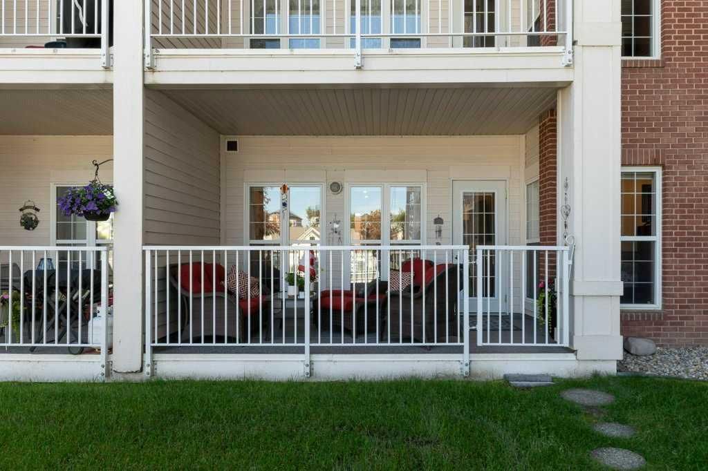 Apartment balcony with white railing, red chairs, and sliding glass doors overlooking a grassy lawn