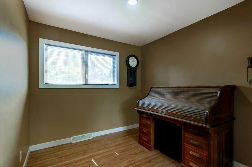 Empty room with brown walls, wood floor, a window, and a dark fireplace mantel.