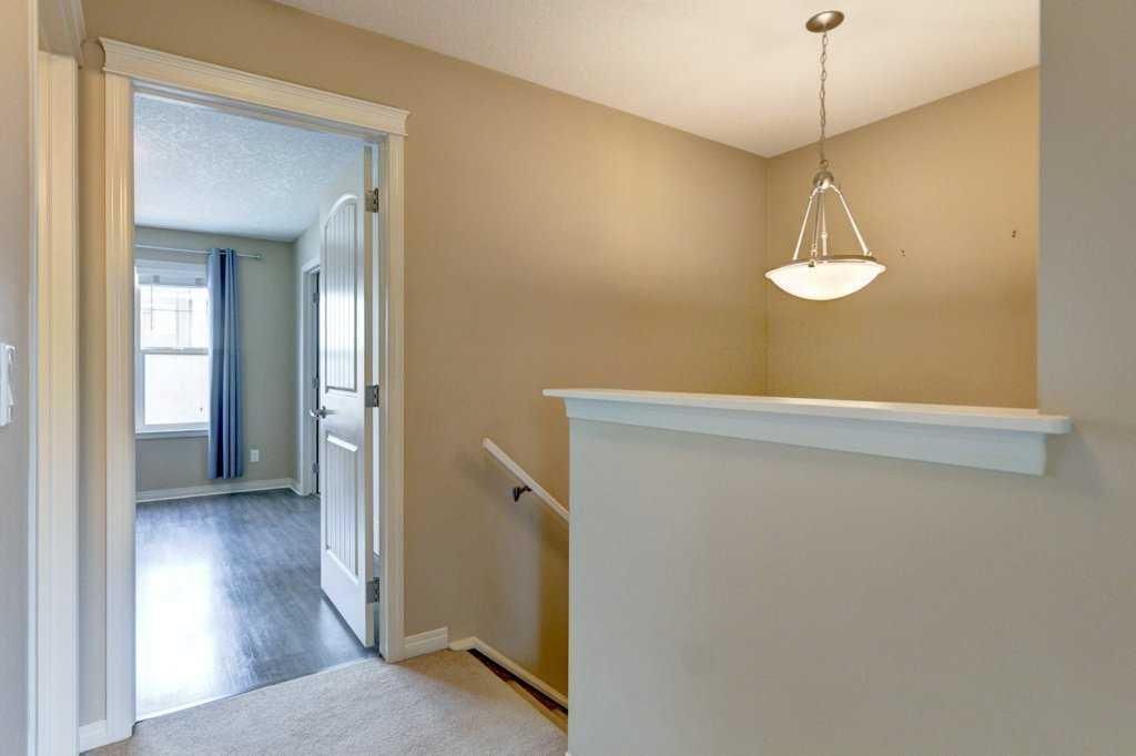 Hallway landing with beige walls, white trim, stair rail, and hanging light near an open doorway