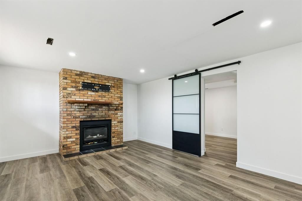 Empty living room with white walls, wood-look floors, brick fireplace, and sliding closet door