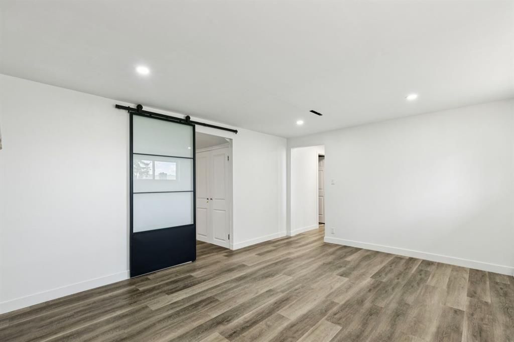 Empty modern room with white walls, wood-look floors, recessed lights, and sliding closet doors