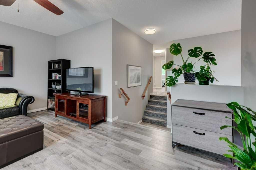Living room with TV, staircase, and white dresser, accented by green plants and gray wood flooring