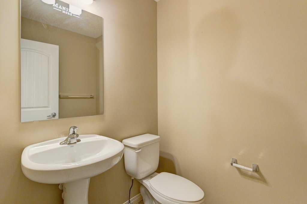 Small beige bathroom with pedestal sink, toilet, mirror, and towel bar.