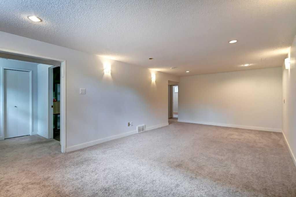 Empty beige living room with carpet, recessed lights, and an open doorway to a hall
