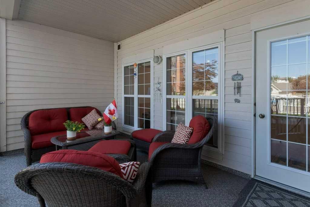 Covered porch with red and black wicker seating, potted flowers, and a glass door.