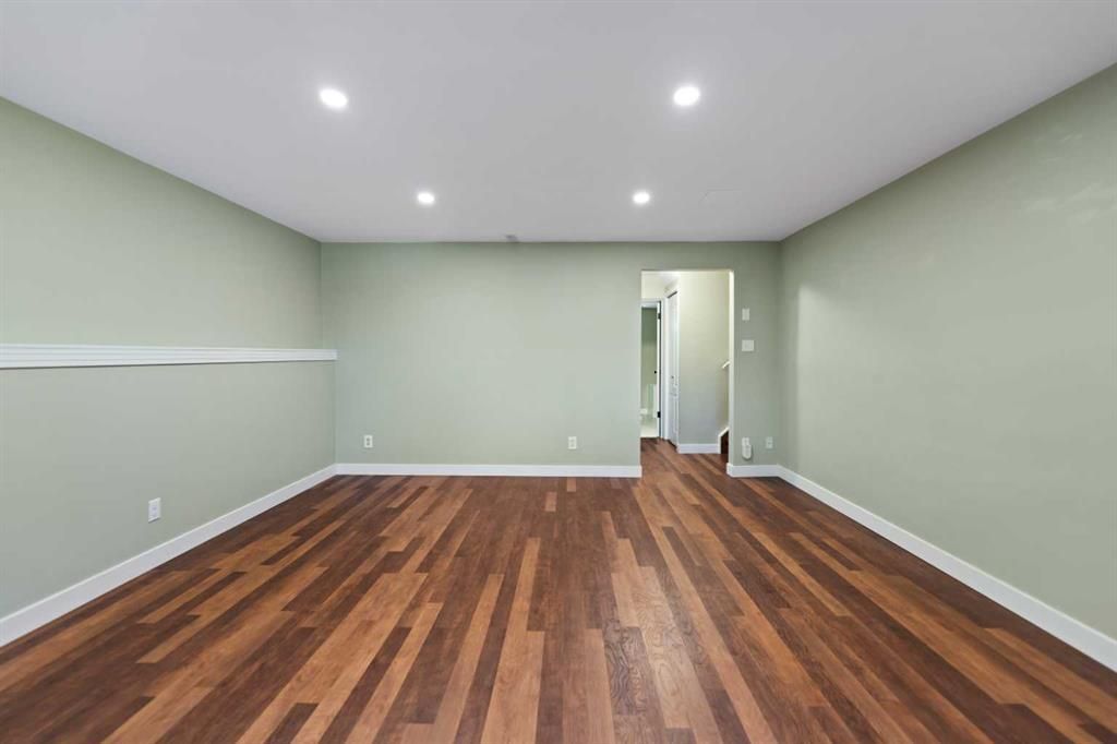 Empty room with wood flooring, pale green walls, recessed ceiling lights, and a doorway at the back